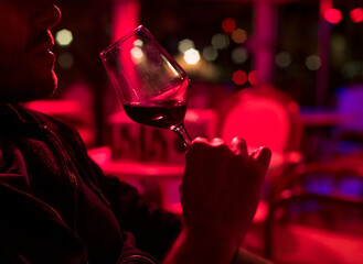 Man drink red wine in a club sitting at table.
