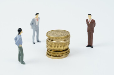 Coins lie on a white surface, miniature figures of businessmen stand nearby - they look at the coins