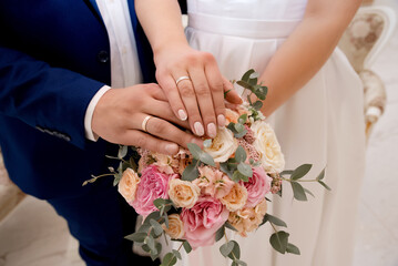 The bride and groom in wedding suits hold a wedding bouquet of white and pink roses. Men's blue...