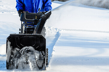 Man using a snow blower to clear a residential driveway