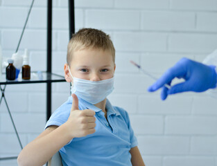 Close-up of a boy in a blue T-shirt and a medical mask, who raised his finger up after vaccination....