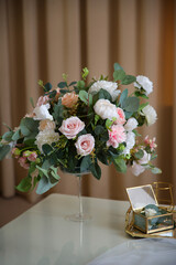 A bouquet of white and pink roses stands on the table in the composition next to the metal structure of the box