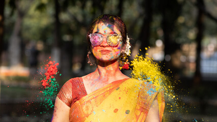 Holi festival of color, Splashing dry organic color or colour or gulal or abeer or Holi powder on a beautiful young girl woman lady in indian attire saree playing celebrating enjoying holi