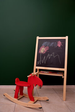 Red wooden rocking horse on a green background next to a drawing board