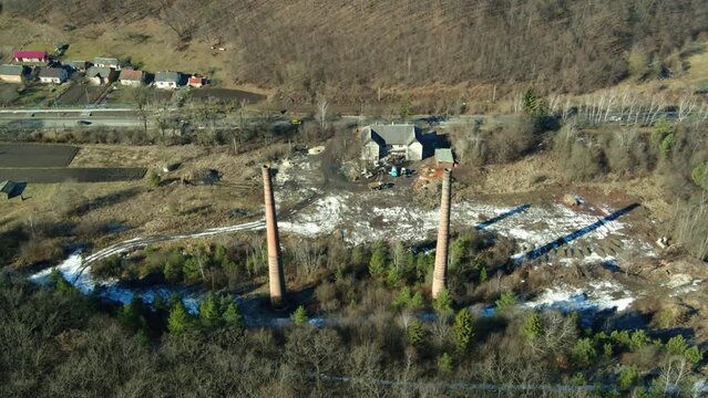 Two large non-working factory smoke pipes, a view from above, cars driving down the road nearby. Abandoned industrial zone in the countryside. Chimney shafts in a small town in winter.