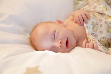 A newborn baby smiles lying on a pillow in a sunbeam close-up