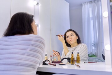 Beautiful middle aged woman doing makeup in front of a mirror.