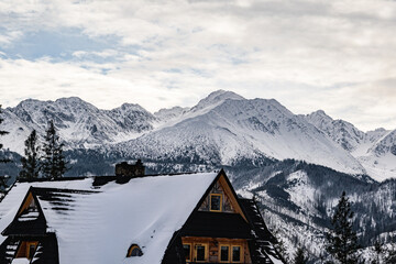 Fototapeta premium Beautiful view of polish Tatra mountains in winter scenery. In the foreground there is a mountain hut situated among trees, in the background there is a view on the highest peaks of Tatra mountains.
