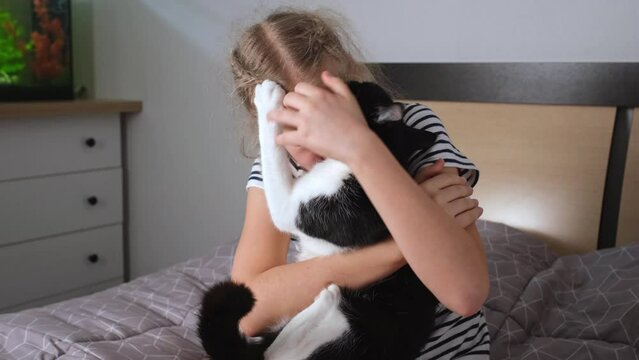 Teenage Girl hugging and kissing black and white cat. Cat scratching and biting girl face and runs away, she crying covering face with hands. Tears and cry of child because of resentment and pain.