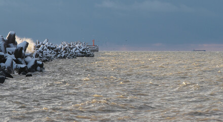 The beginning of a storm, the sea is seething and the breakwater is covered with snow.