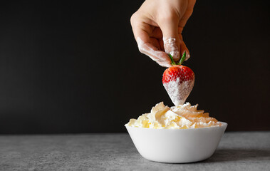 Hand dipping strawberry fruit in whipped cream bowl
