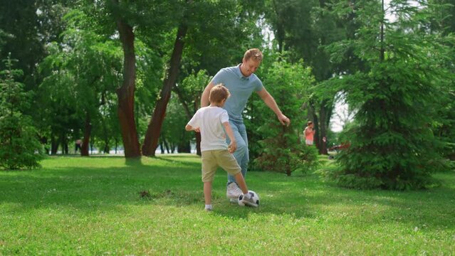 Happy father teaching son play soccer. Cheerful boy passing ball to dad on lawn.