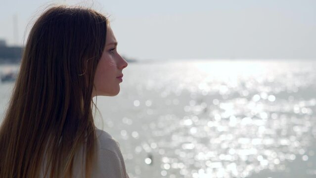 Profile of a beautiful sad and lonely girl in front of the sea during sunset. She is heartbroken.