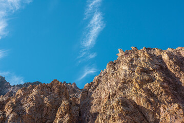 Scenic mountain landscape with sharp rocks under blue sky in sunny day. Colorful scenery with gold sunlit sharp rocky mountains. Sharp rocks in bright sun. High rocky mountains in golden sunlight.