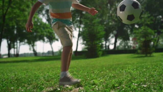 Active boy kick ball on green grass. Little sportsman play football in park.