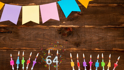 Top view, birthday decorations from letters of candles with fire and festive garlands, save space. Happy birthday background with number 64 on a brown board table. happy birthday to sixty four.