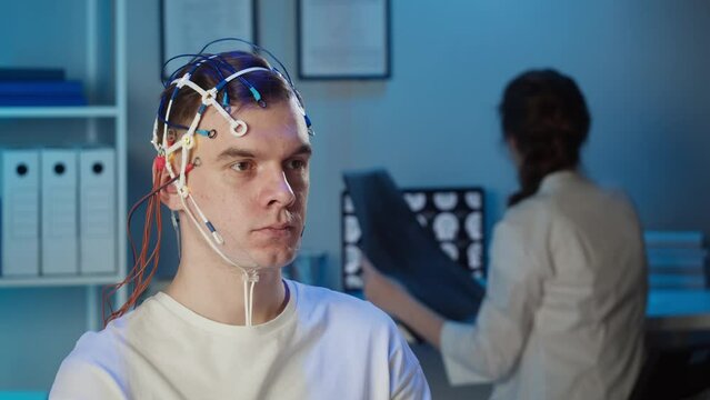 Man wearing EEG topographer for examining brain, doctor making electrogram of scalp activity. Researching of brain work using electroencephalography headset.