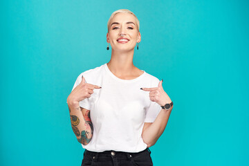 Make it your own. Studio shot of a confident young woman pointing at her t shirt against a turquoise background.