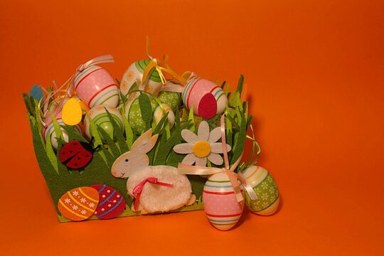 Easter, a basket filled with painted eggs, the front of the basket bunny and a ladybug, all on an orange  background.