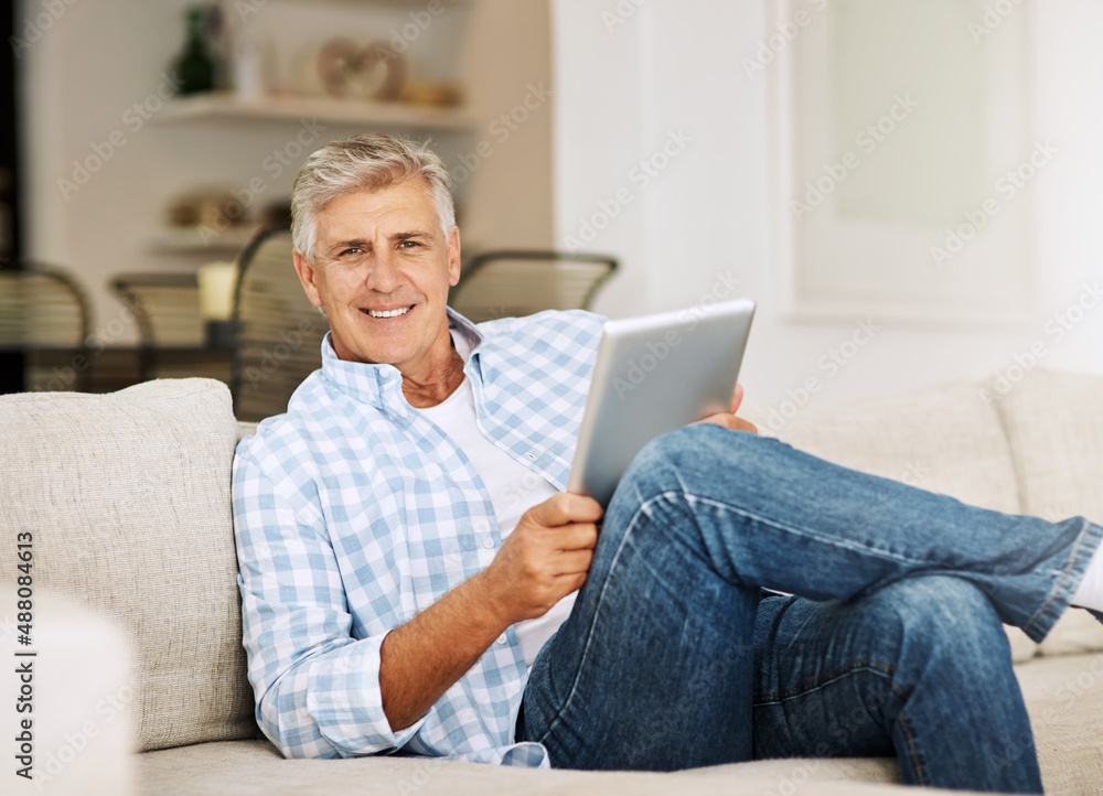 Poster killing time online. shot of a mature man using his digital tablet while relaxing on his sofa at hom