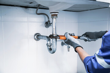 Technician plumber using a wrench to repair a water pipe under the sink. Concept of maintenance, fix water plumbing leaks, replace the kitchen sink drain, cleaning clogged pipes is dirty or rusty. - obrazy, fototapety, plakaty