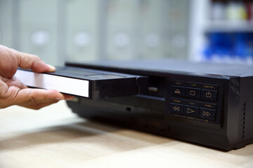 Close-up hand put or insert video cassette tape VHS old retro style on video record playback concept of vintage electric and electronic appliances multimedia player device old fashioned.