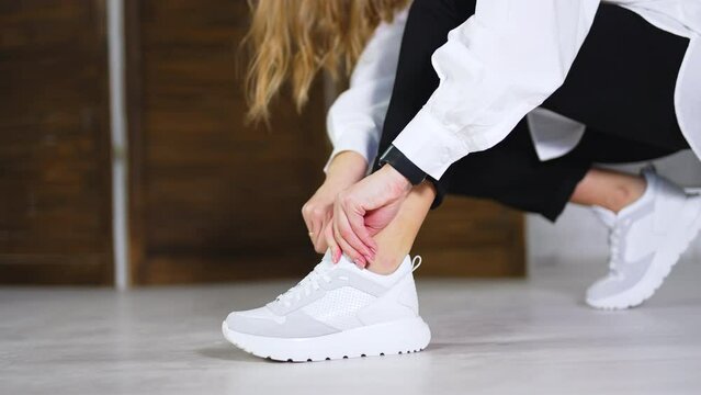 Female model demonstrates new white sneakers. Lady tying the laces on a footwear. Close up. Blurred backdrop.