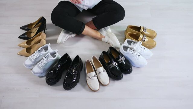 Woman sitting on the floor counts the pairs of shoes in front of her. Variety of footwear presentation. View from top.