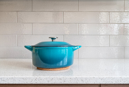 Turquoise enameled cast iron covered round dutch oven on a granite counter top against a ceramic background
