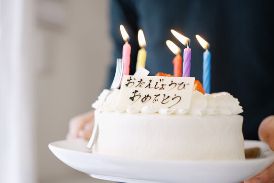 日本語で誕生日おめでとうと書かれているケーキを運ぶアジア人のお父さん