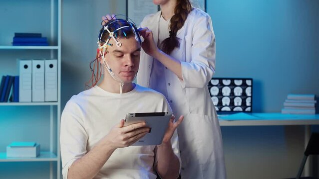 EEG topographer for examining brain, doctor making electrogram of scalp activity. Researching of brain work, man using gadget wearing electroencephalography headset.