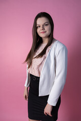 A cute plus-size model stands on a pink background in a white unbuttoned jacket, a pink blouse with lace, a black office skirt and high-heeled shoes. A modest business portrait