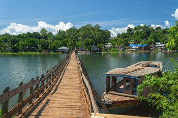 A small boat leans on a long bridge over the water, which connects two villages separated  by lake Aranio, South Borneo, Indonesia.
