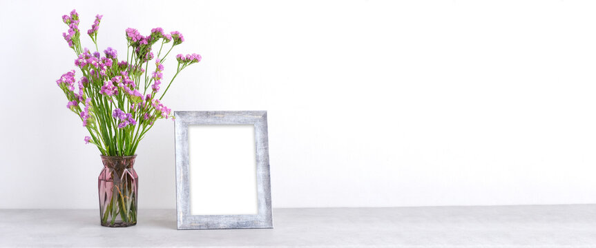 Flower bouquet in glass vase and blank grey vintage wooden frame on table background with copy space , Banner for mock up, template