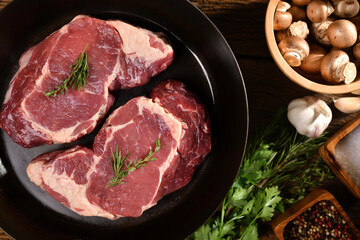 Top view of raw steak beef meat on a pan on a wooden table with side vegetables prepared for cooking.