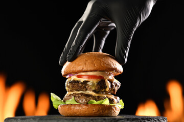 Hand putting top burger bun on a meat double cheeseburger with vegetables with sauce oozing and...