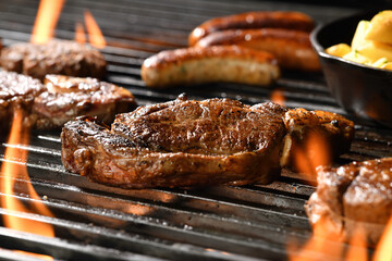 Cooked juicy steak meat beef with seasoning on a flaming grill surrounded by other meat and...