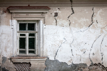 Window on the old wall. The plaster on the wall is crumbling and cracks have appeared. The plastered wall of the old house is crumbling.