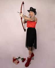 Beautiful Italian model with tattoos holding a bow and arrow  shooting someone in a cowboy hat and a blouse 