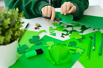Fototapeta premium DIY St.Patricks Day decor. A boy cuts with scissors craft card of shiny green paper. Selective focus