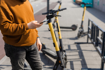 Close up guy is paying for electrical scooter by web payment using his mobile phone. Modern urban transport concept