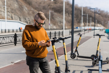Guy is paying for electrical scooter by web payment using his mobile phone. Modern urban transport concept
