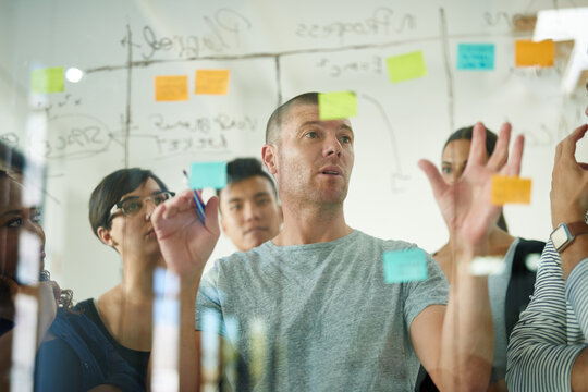 Planning is the first step. Cropped shot of a group of young designers planning on a glass board.