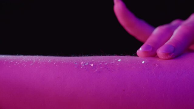 Hand skin in pink neon light, female human body part and ultraviolet, touching arm surface macro shooting, putting glitter shimmer.