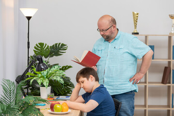 Dad reads a book and helps his son with his school assignment.