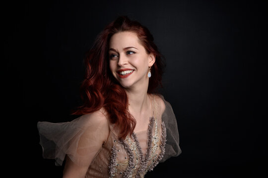portrait of pretty female model with red hair wearing glamorous fantasy tulle gown and crown.  Posing with a moody dark background.