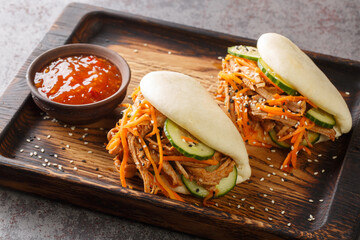 Street food bao sandwiches with pulled pork and vegetables close-up on a wooden tray on the table....