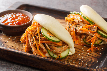 Delicious steamed bao buns sandwiches with pulled pork close-up on a wooden tray on the table....