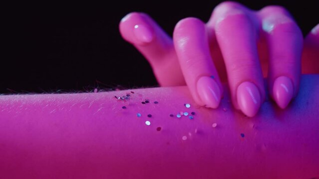 Hand skin in pink neon light, female human body part and ultraviolet, touching arm surface macro shooting, putting glitter shimmer.