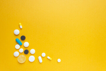 Group of multicolored pills and capsules in the lower left corner. Yellow background. Healthcare and longevity concept.